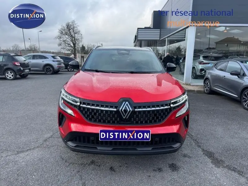 Vue avant d'un Renault Austral rouge flamme avec calandre noire et logo Renault central, stationné devant un showroom.