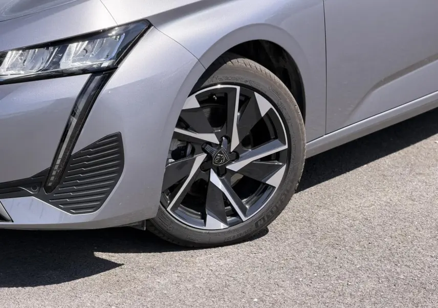 Gros plan sur la roue avant droite et le pare-chocs avant gris Artense d'une Peugeot 308 Hybrid 2025.