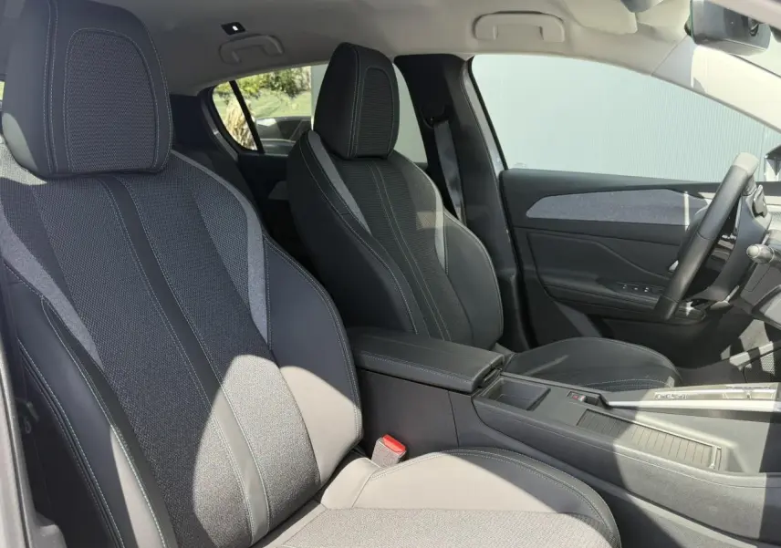 Vue intérieure côté droit de la Peugeot 308 Hybrid 2025 montrant les sièges tissu et cuir gris avec accoudoir central.