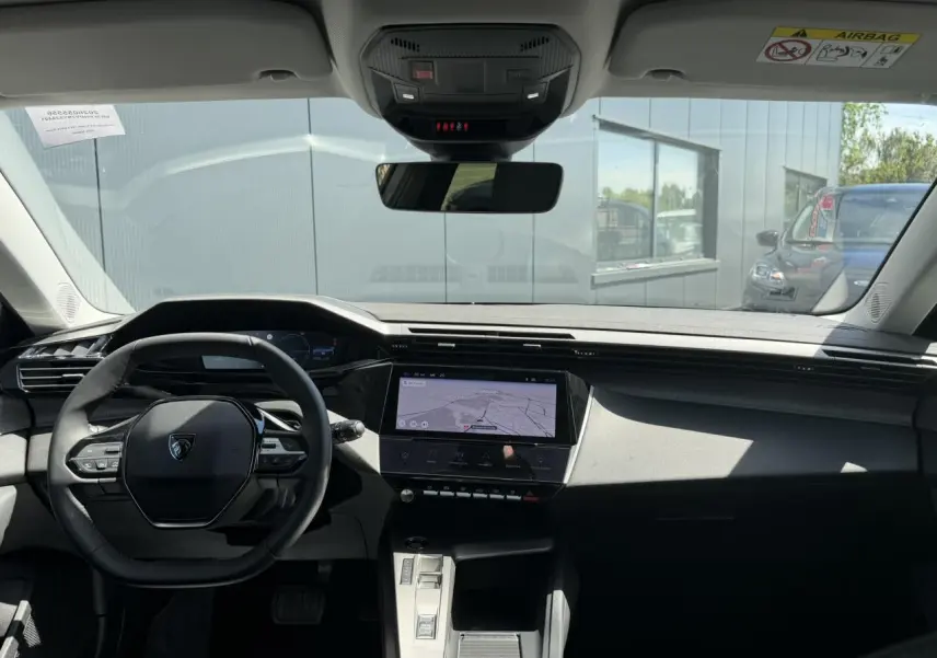 Vue intérieure avant du Peugeot 308 Hybrid 2025, tableau de bord noir avec écran tactile central affichant la navigation.
