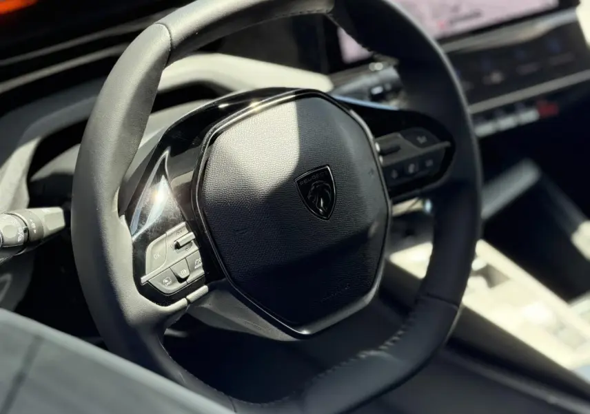 Gros plan sur le volant en cuir noir du Peugeot 308 Hybrid 145, avec commandes intégrées et logo central.