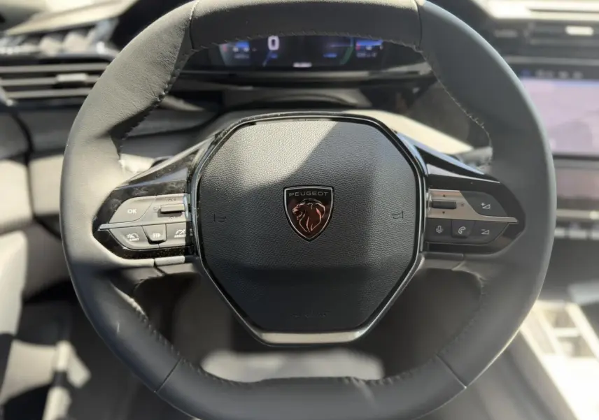 Vue rapprochée du volant cuir noir de la Peugeot 308 Hybrid 145 avec commandes intégrées et logo lion central.