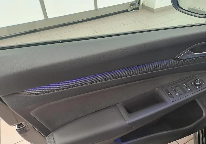 Détail de la porte côté conducteur de la Volkswagen Golf 2.0 TDI 150 DSG7 R Line noire avec éclairage d'ambiance bleu.