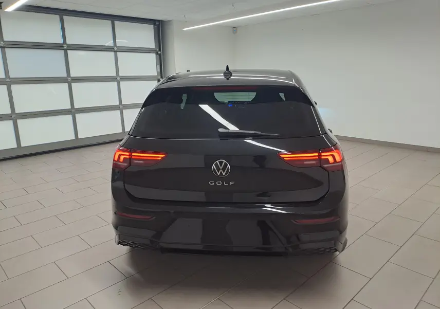 Vue arrière d'une Volkswagen Golf 2.0 TDI 150 DSG7 R Line noire grenadille avec feux allumés dans un garage.