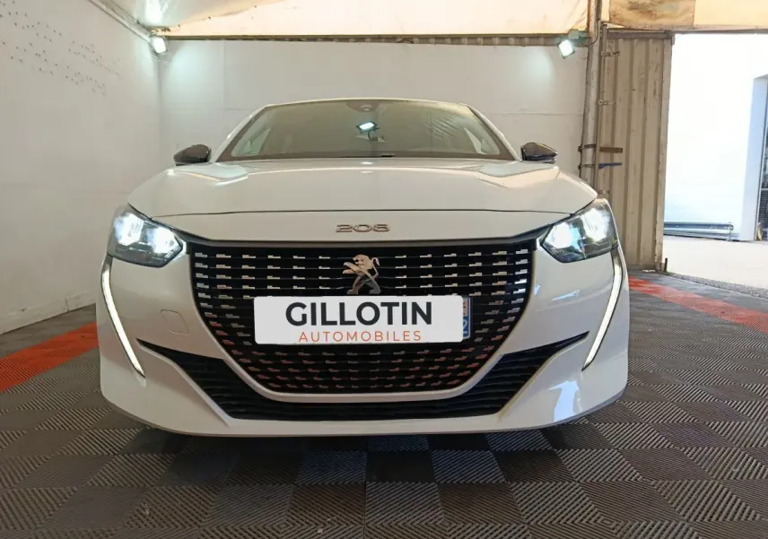 Vue frontale d'une Peugeot 208 blanche 2023 avec phares LED allumés et calandre noire distinctive.