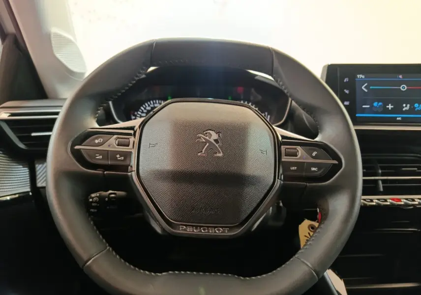Vue rapprochée du volant cuir multifonctions noir d'une Peugeot 208 2023 avec tableau de bord et écran tactile visible à droite.