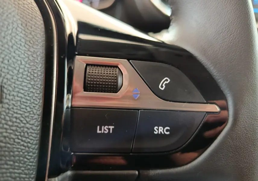 Gros plan sur les commandes multifonctions en cuir du volant côté gauche d'une Peugeot 208 blanche 2023.