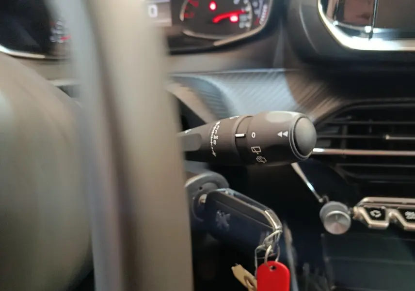 Détail intérieur du tableau de bord de la Peugeot 208 blanc, avec clé insérée et commandes au volant visibles.