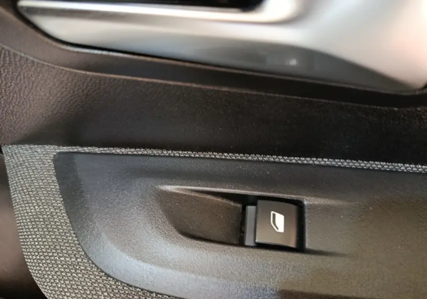 Gros plan sur le bouton de commande de la vitre électrique côté conducteur d'une Peugeot 208 blanche 2023.