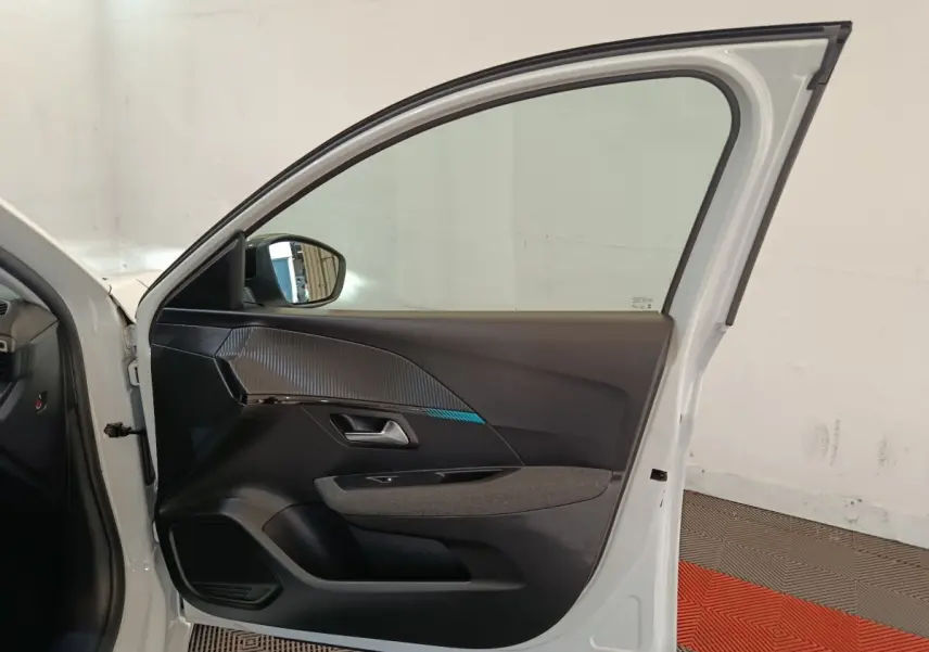 Vue intérieure de la porte avant gauche blanche d'une Peugeot 208 2023 avec garniture noire et détails texturés.