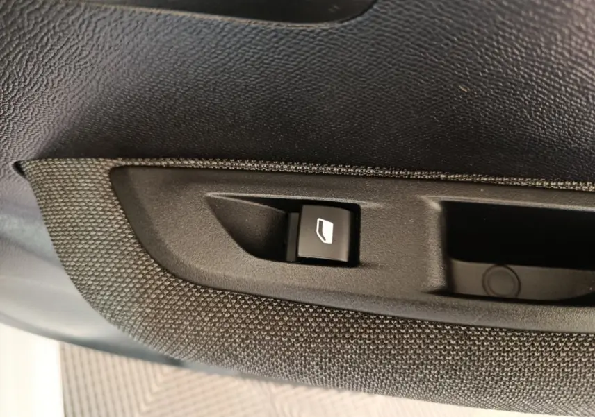 Gros plan sur le bouton de commande de lève-vitre intégré dans la garniture noire texturée d’une Peugeot 208 blanche.