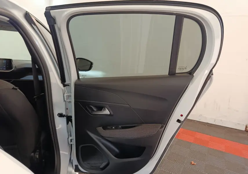 Vue de profil de la porte arrière droite blanche d'une Peugeot 208 2023 avec garniture intérieure noire et tissu gris.