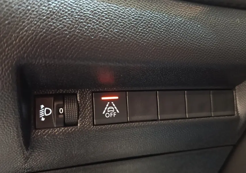 Gros plan sur les commandes de réglage des phares et désactivation de l’aide au maintien de voie dans une Peugeot 208 blanche.