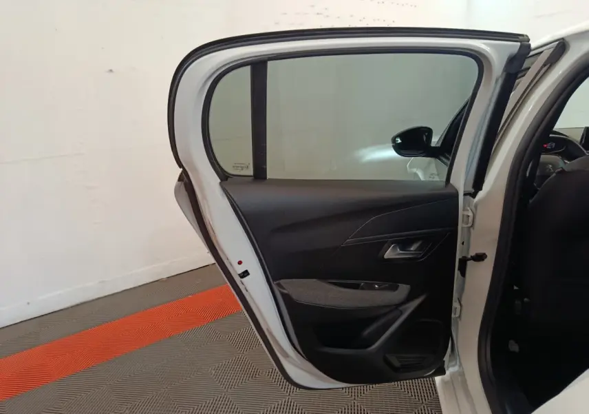 Vue intérieure de la porte arrière droite ouverte d'une Peugeot 208 blanche, avec garniture noire et fenêtre teintée.