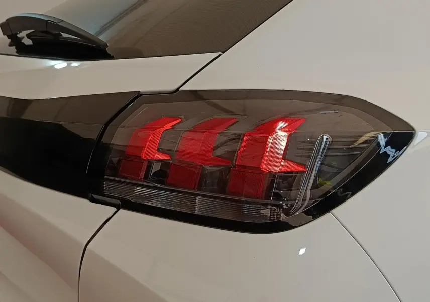 Gros plan sur le feu arrière droit rouge d'une Peugeot 208 blanche, soulignant le design moderne du véhicule.