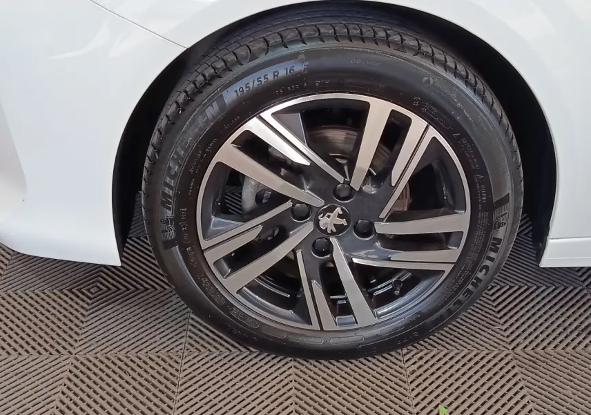 Gros plan sur la roue avant droite d'une Peugeot 208 blanche, avec jante alliage bicolore et pneu Michelin.