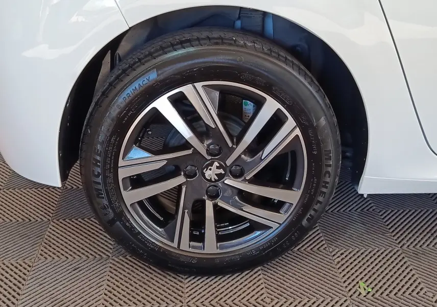 Gros plan sur la roue avant droite d'une Peugeot 208 blanche, jante alliage bicolore et pneu Michelin.