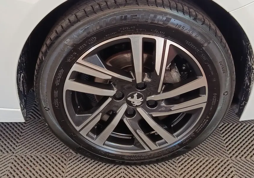 Gros plan sur la roue avant droite d'une Peugeot 208 blanche, jante alliage noire et argent avec logo lion central.