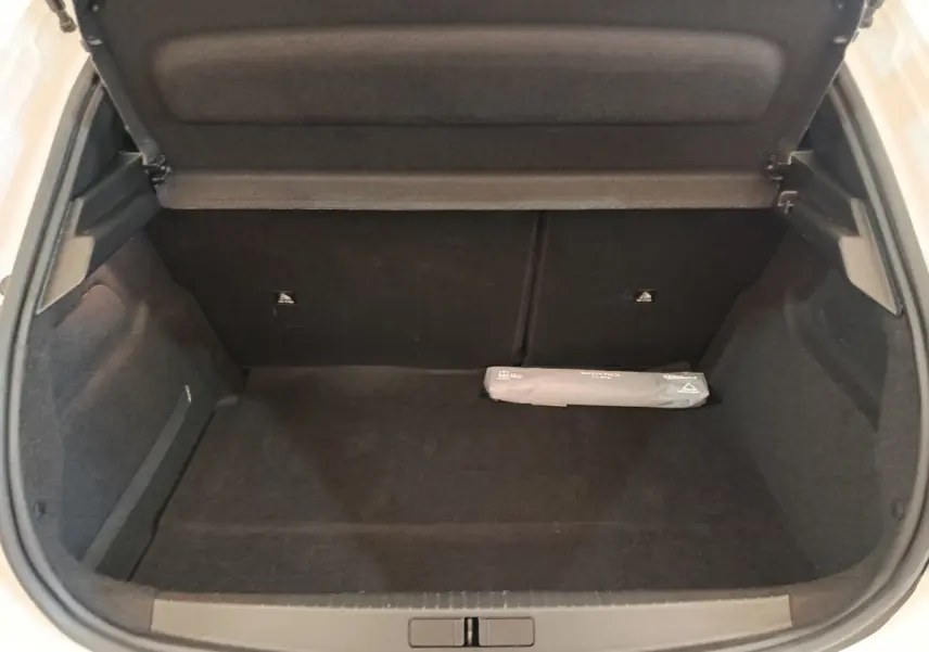 Coffre ouvert d'une Peugeot 208 blanche, vue de l'arrière, montrant un espace de chargement vide avec un kit de sécurité.