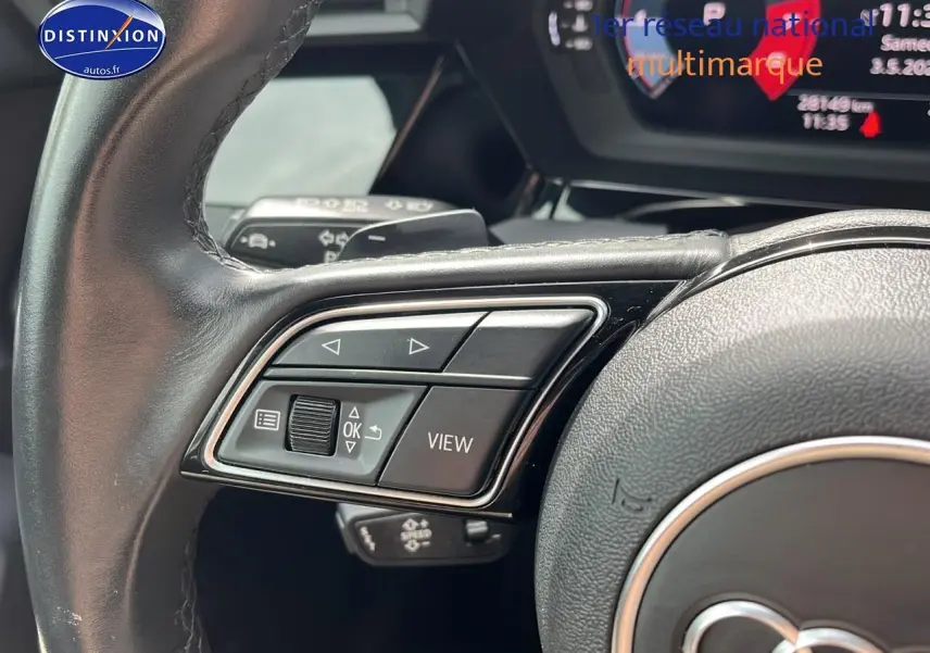 Gros plan sur les commandes gauche du volant cuir multifonction d'une Audi A3 Sportback gris Manhattan 2023.