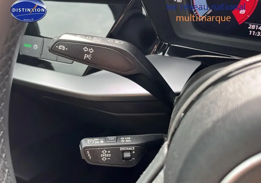 Gros plan sur les commandes au volant d'une Audi A3 Sportback 2023 gris Manhattan, affichage digital partiel visible.
