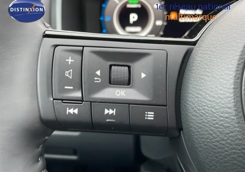 Gros plan sur les commandes multifonctions à gauche du volant du Nissan Qashqai blanc nacré 2025, avec tableau de bord numérique en arrière-plan.