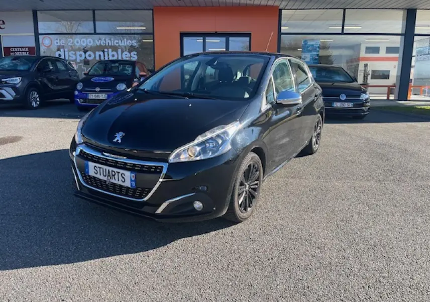 Peugeot 208 noire vue 3/4 avant droit, avec jantes noires et calandre chromée, stationnée devant un bâtiment commercial.