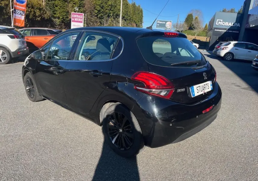 Peugeot 208 noire vue 3/4 arrière droit, avec feux arrière distinctifs et jantes noires, stationnée en extérieur.