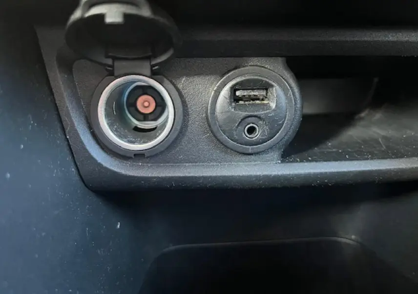 Prise 12V et port USB en gros plan sur la console centrale d'une Peugeot 208 noire de 2017.