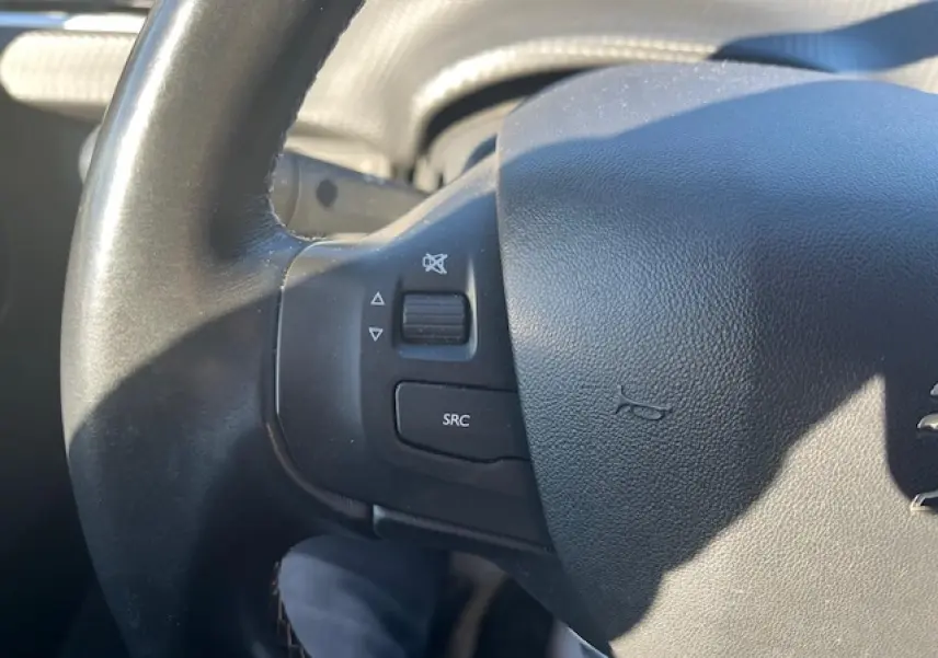 Gros plan sur le volant noir multifonction de la Peugeot 208 2017, avec commandes audio visibles à gauche.