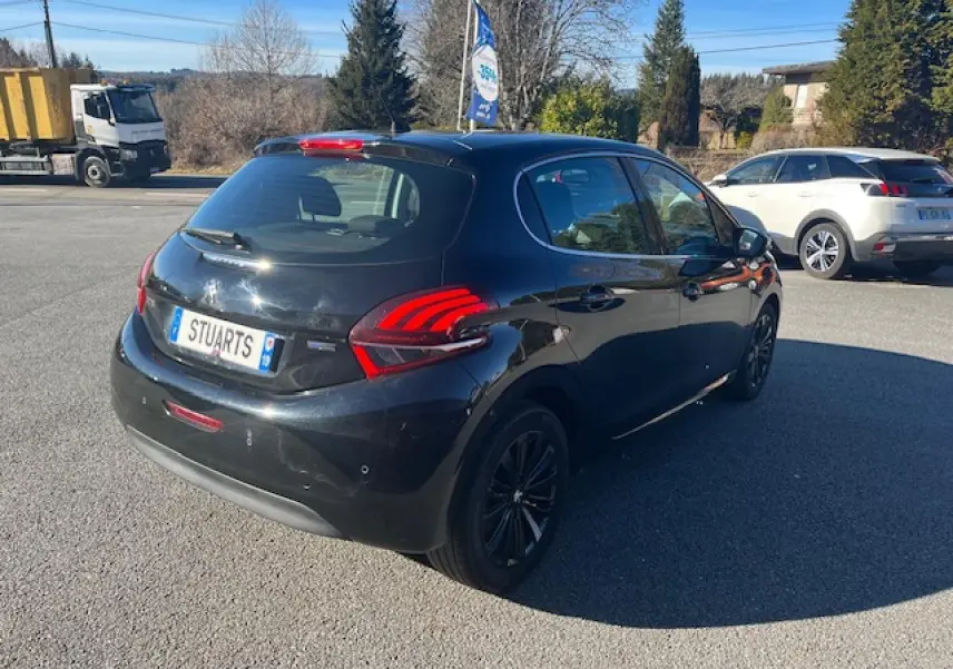 Peugeot 208 noire vue en 3/4 arrière droit, avec feux arrière distinctifs et jantes noires sur parking extérieur.