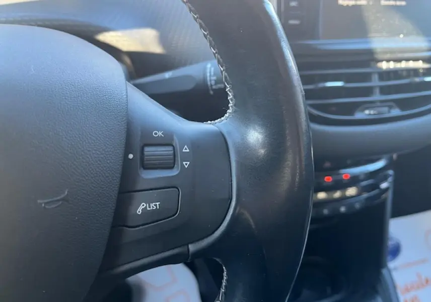Gros plan sur le volant noir multifonction de la Peugeot 208 2017 avec commandes intégrées et tableau de bord flou en arrière-plan.