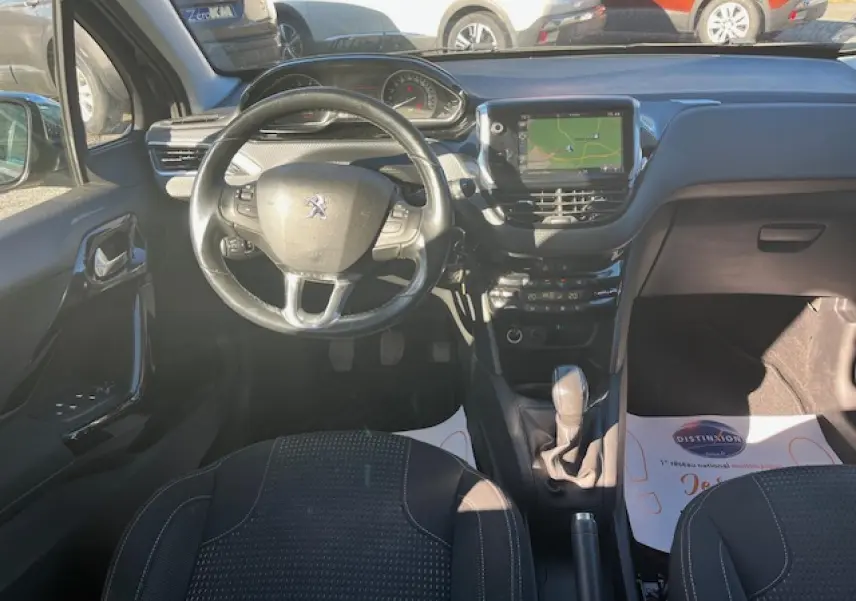 Vue intérieure avant de la Peugeot 208 noire, montrant le volant multifonction, écran tactile et levier de vitesse manuel.