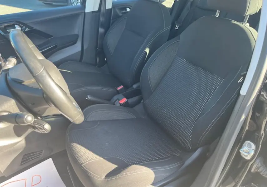 Vue intérieure côté conducteur de la Peugeot 208 noire, montrant les sièges avant en tissu et le volant multifonction.