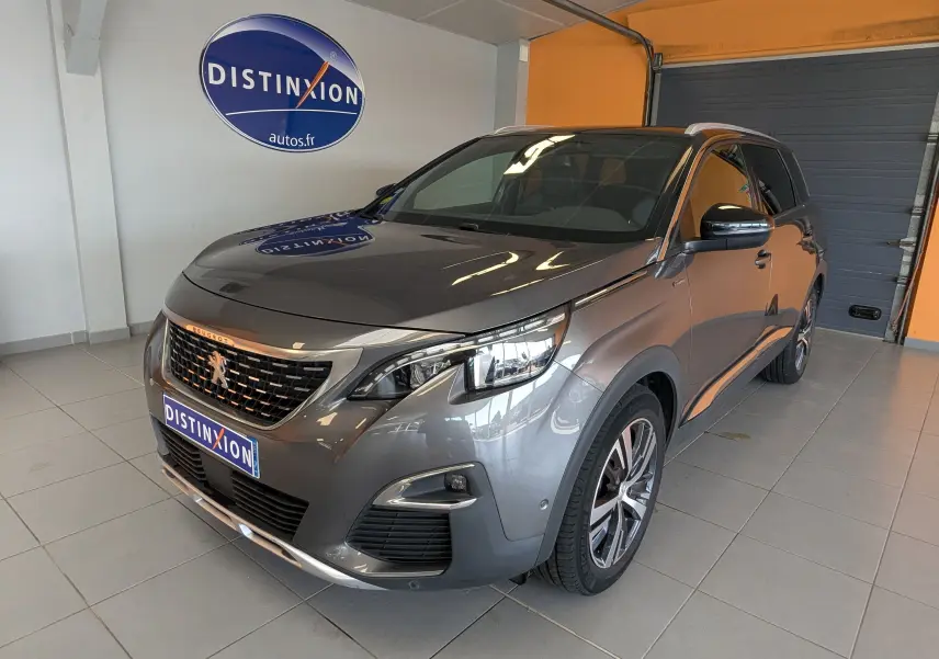 Peugeot 5008 gris 3/4 avant droit en intérieur, avec calandre et jantes spécifiques GT Line visibles.