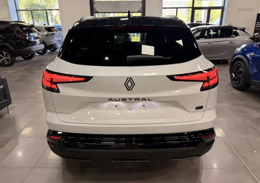 Vue arrière d'un Renault Austral blanc nacré avec toit noir, feux arrière LED et logo central dans un showroom.