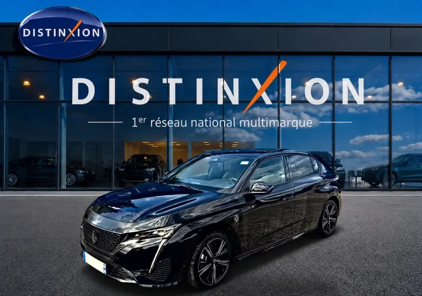 Peugeot 308 1.2 hybrid 145 GT noir vue 3/4 avant, avec jantes alu et calandre distinctive devant un showroom Distinxion.