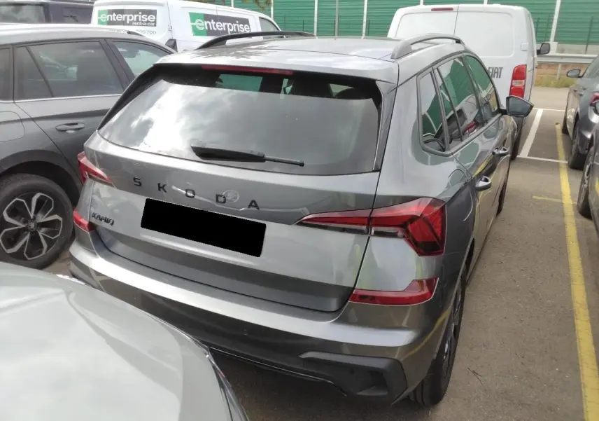 Vue 3/4 arrière d'un Skoda Kamiq gris graphite avec hayon électrique et toit panoramique visible en stationnement.