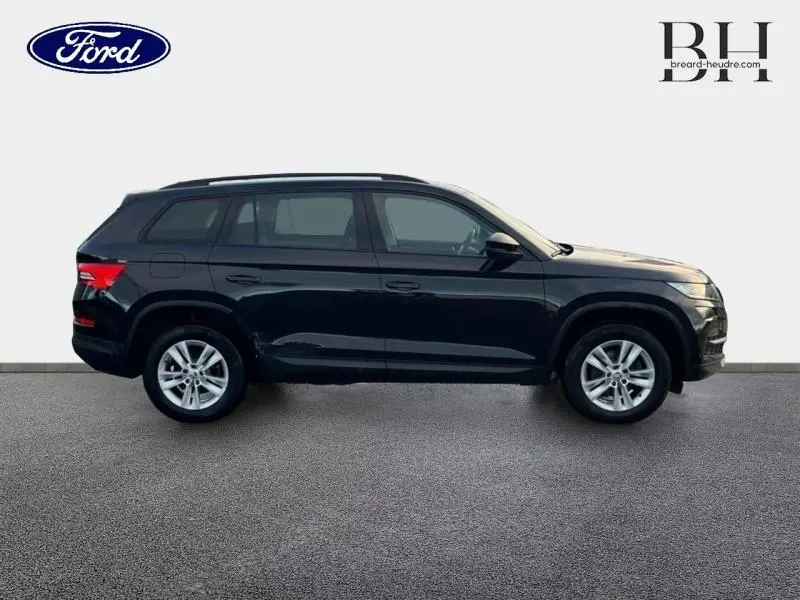 Profil côté gauche d'un SUV SKODA KODIAQ noir Magic Nacré, avec jantes alliage et barres de toit visibles.