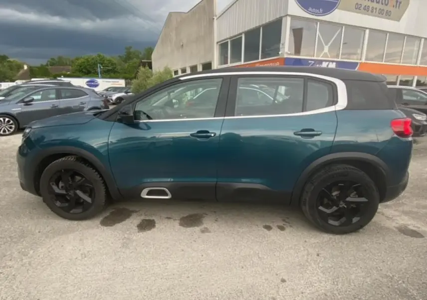 Vue latérale gauche d'un Citroën C5 Aircross bleu Tijuca avec toit noir et jantes alliage noires, stationné en extérieur.