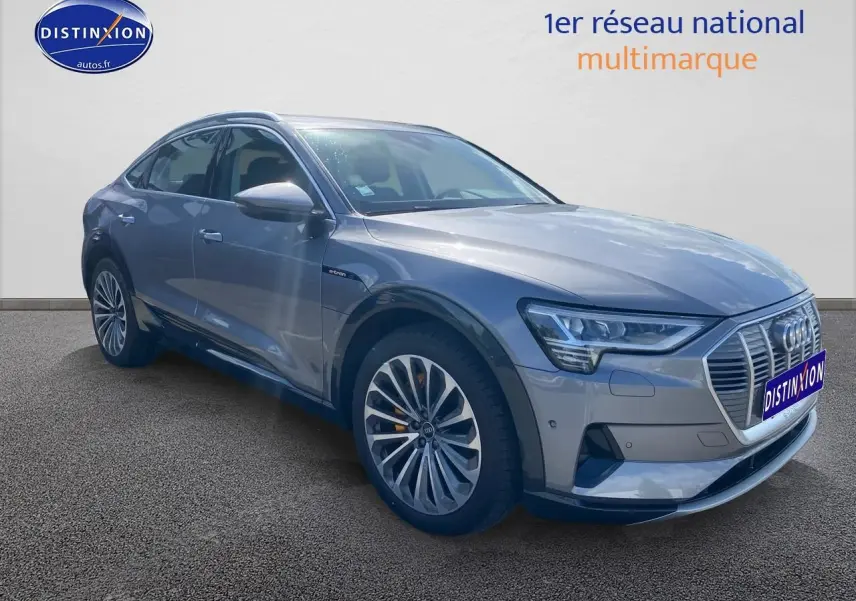 Audi Q8 E-Tron gris en 3/4 avant droit, mettant en valeur sa calandre distinctive et ses jantes alu élégantes.