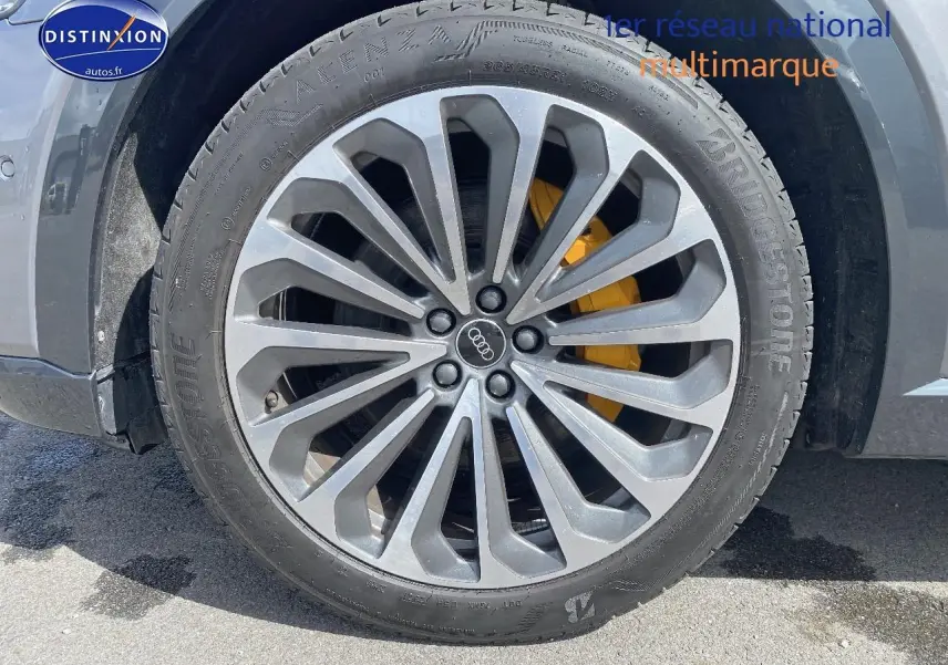 Gros plan sur la jante alu grise avec logo Audi et étrier de frein jaune du côté avant gauche du Q8 E-TRON gris.