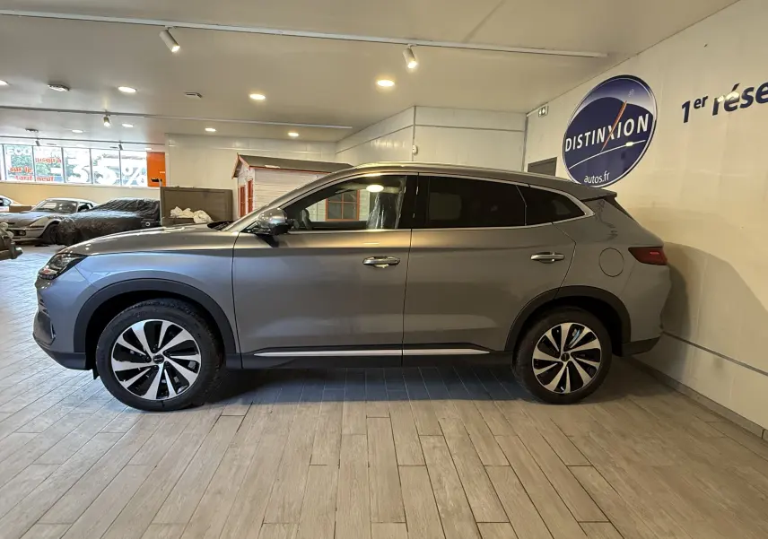 Vue latérale droite du SUV BYD SEAL U gris, hybride rechargeable, avec jantes bicolores et vitres teintées, en intérieur showroom.