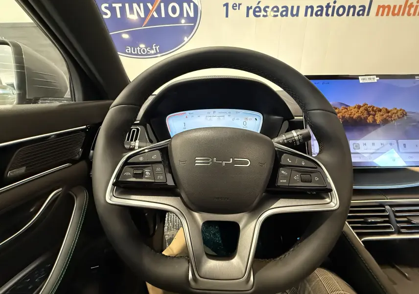 Vue intérieure centrée sur le volant noir du BYD SEAL U avec tableau de bord digital et écran tactile latéral.