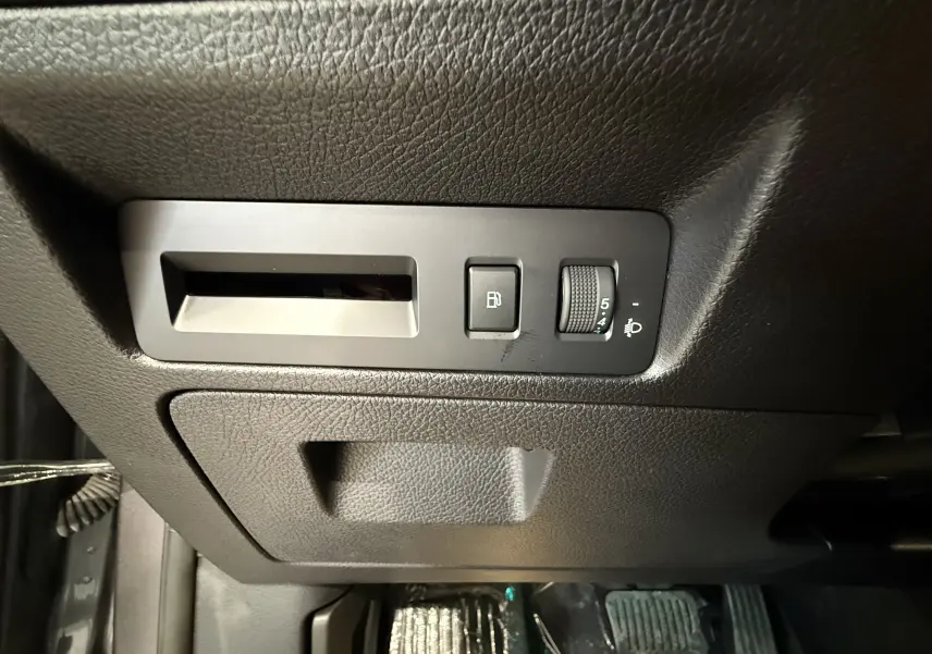Détail intérieur côté gauche montrant les commandes d’ouverture du réservoir et de réglage des phares sur plastique noir texturé.