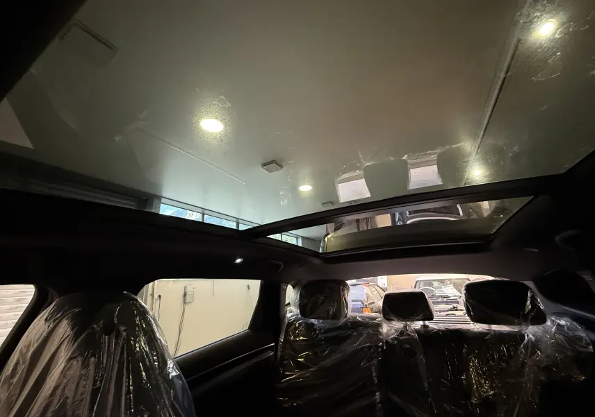 Vue intérieure du toit panoramique en verre du BYD SEAL U gris, avec sièges arrière protégés par des housses plastiques.