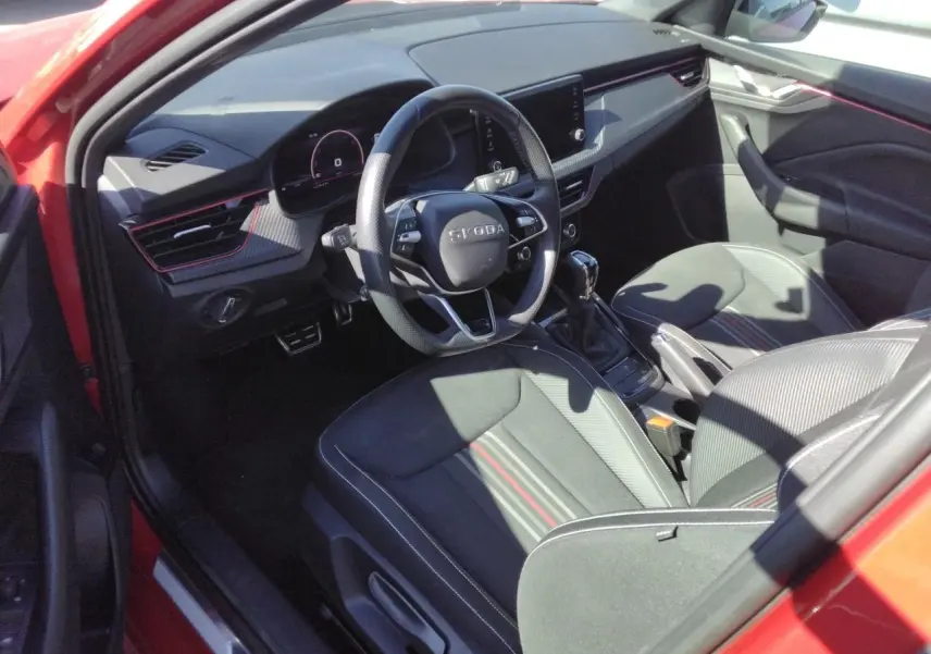 Intérieur côté conducteur du Skoda Kamiq Rouge Velvet, volant sport cuir, inserts carbone et sièges tissu noir à bandes rouges.