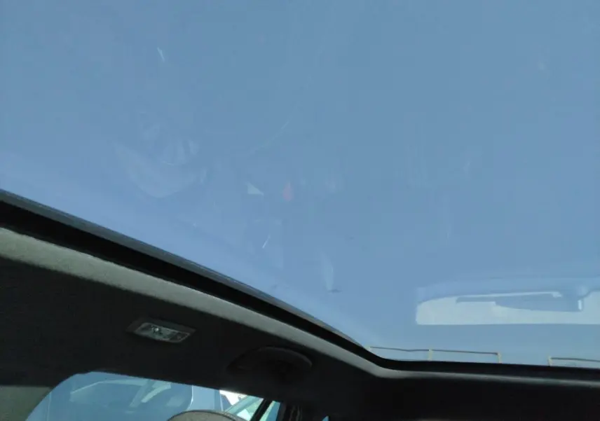 Vue intérieure montrant le toit panoramique noir du Skoda Kamiq Rouge Velvet avec ciel bleu visible à travers le verre.