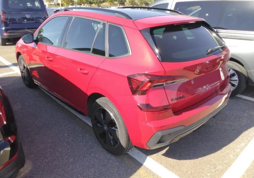 Vue 3/4 arrière droite d’un Skoda Kamiq rouge Velvet avec jantes noires et toit panoramique, stationné en extérieur.