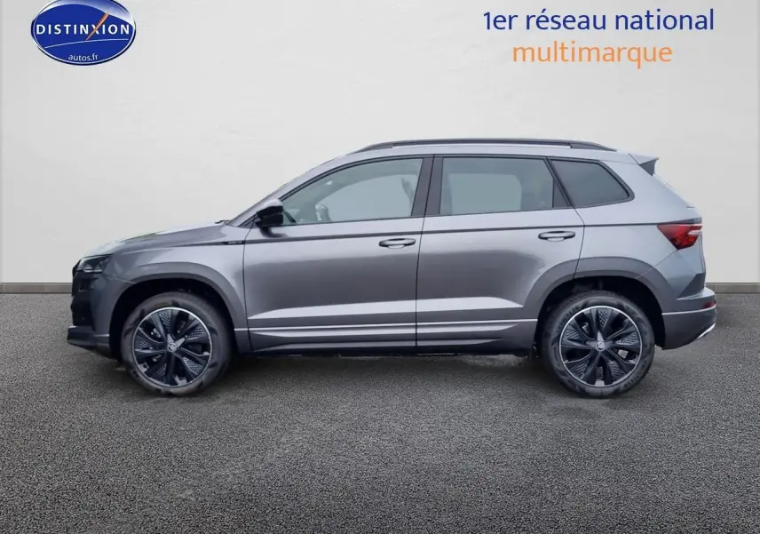 Profil côté gauche d'un SUV SKODA KAROQ gris graphite 2025 avec jantes alu et barres de toit visibles.